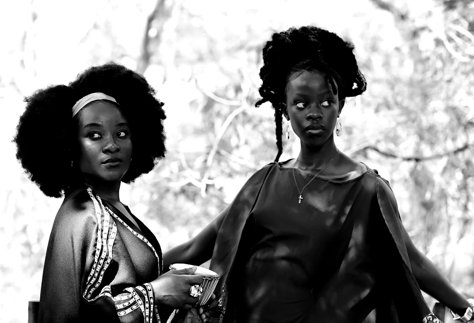 Two women in the shade of a tree, one in beadwork, in black and white.